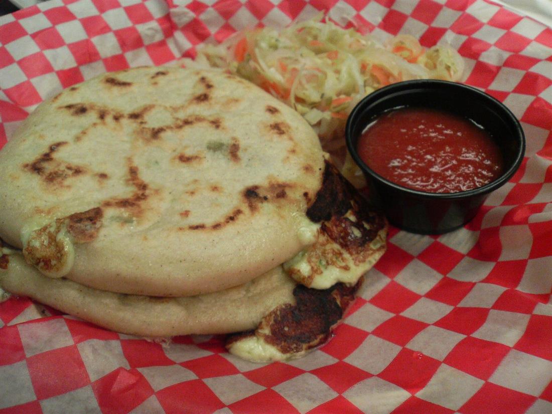 Dos pupusas de queso con curtido y salsa sobre papel de cuadros rojos